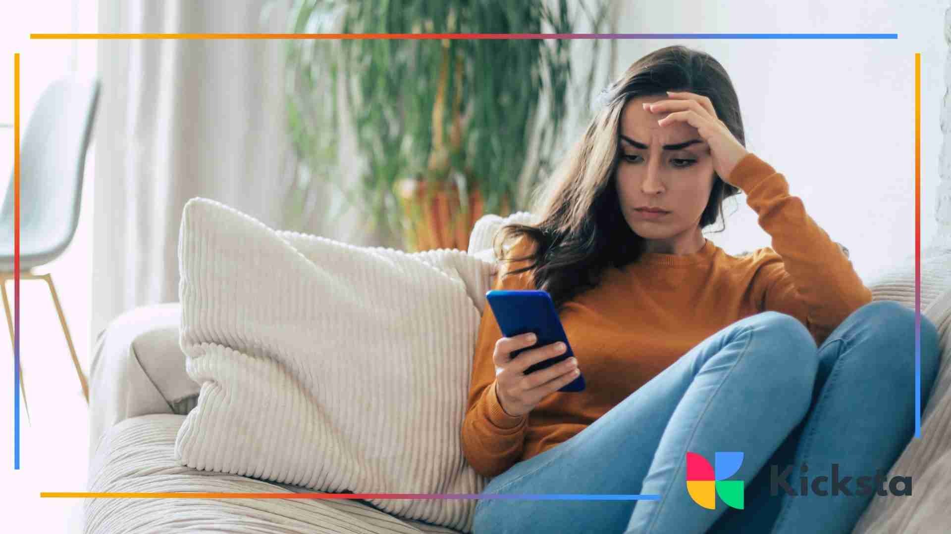 Woman sitting on a couch looking concerned while checking her phone.