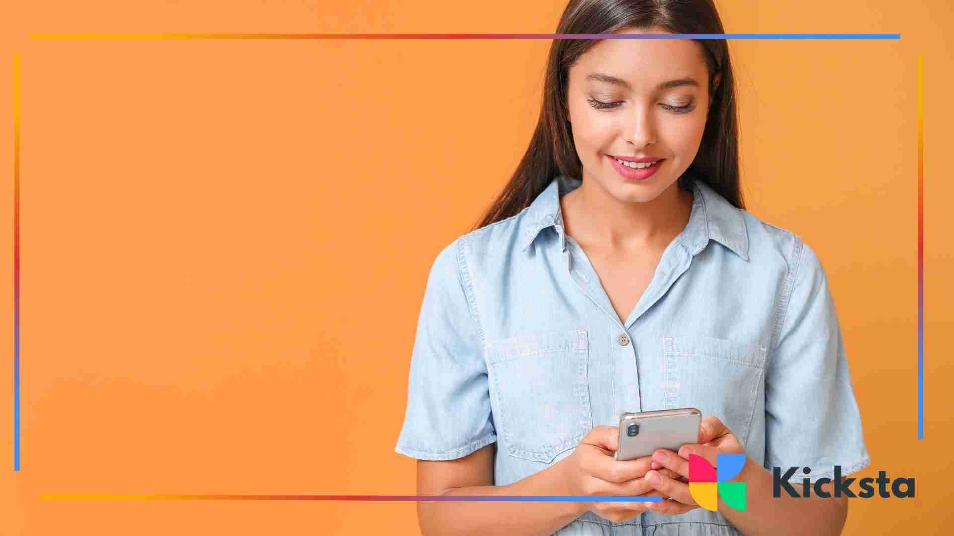 Woman smiling while looking at her smartphone against an orange background.