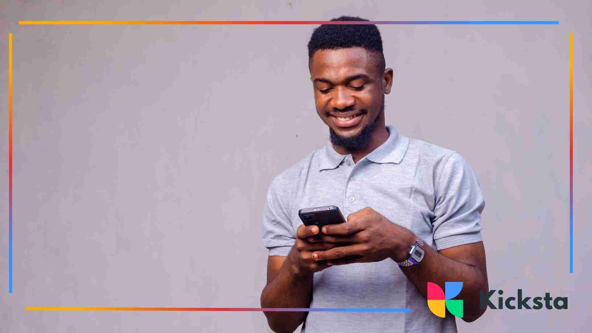 Man smiling while typing on a smartphone against a plain background.