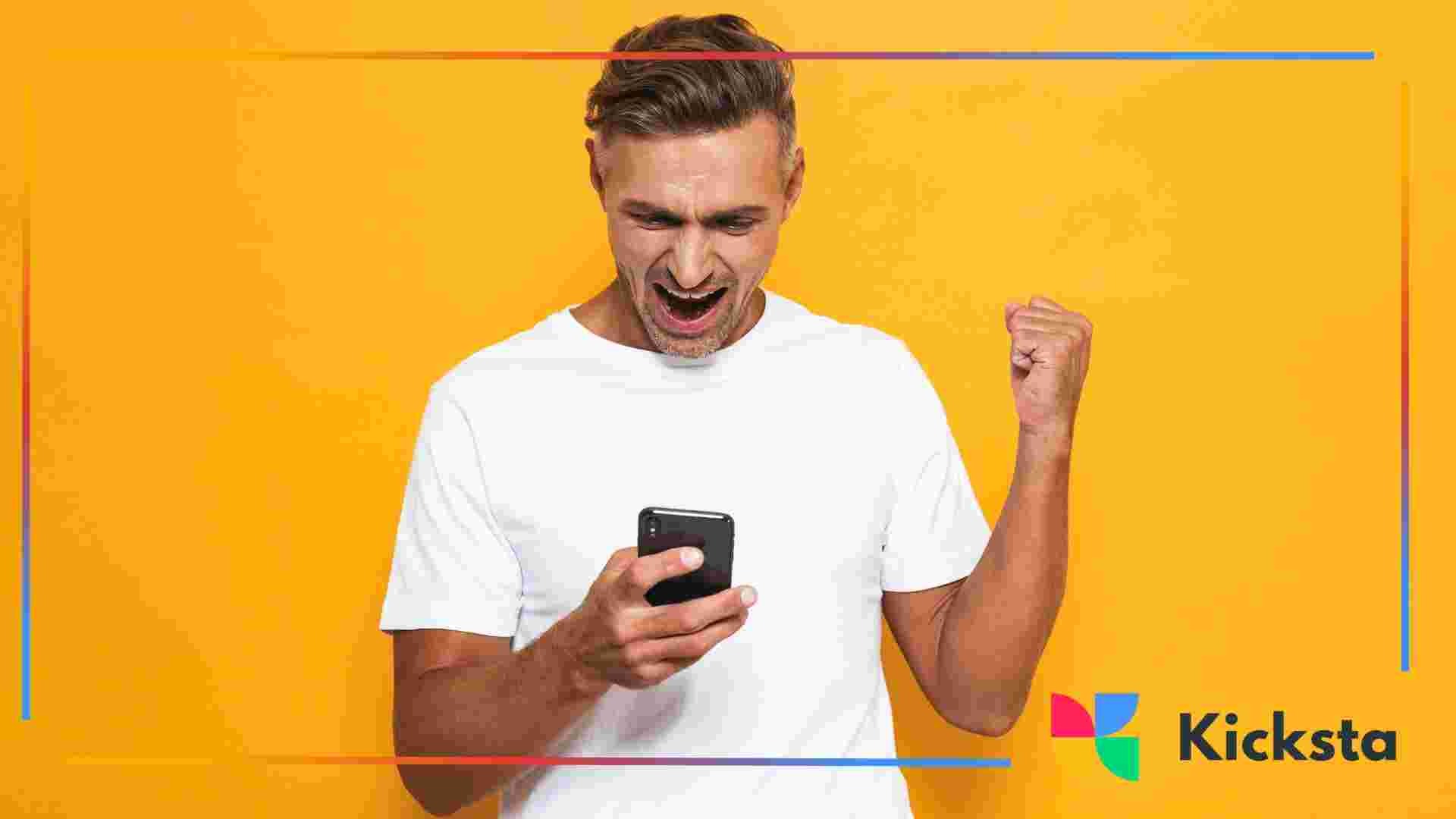 Person smiling and raising a fist while looking at a smartphone against a yellow background.