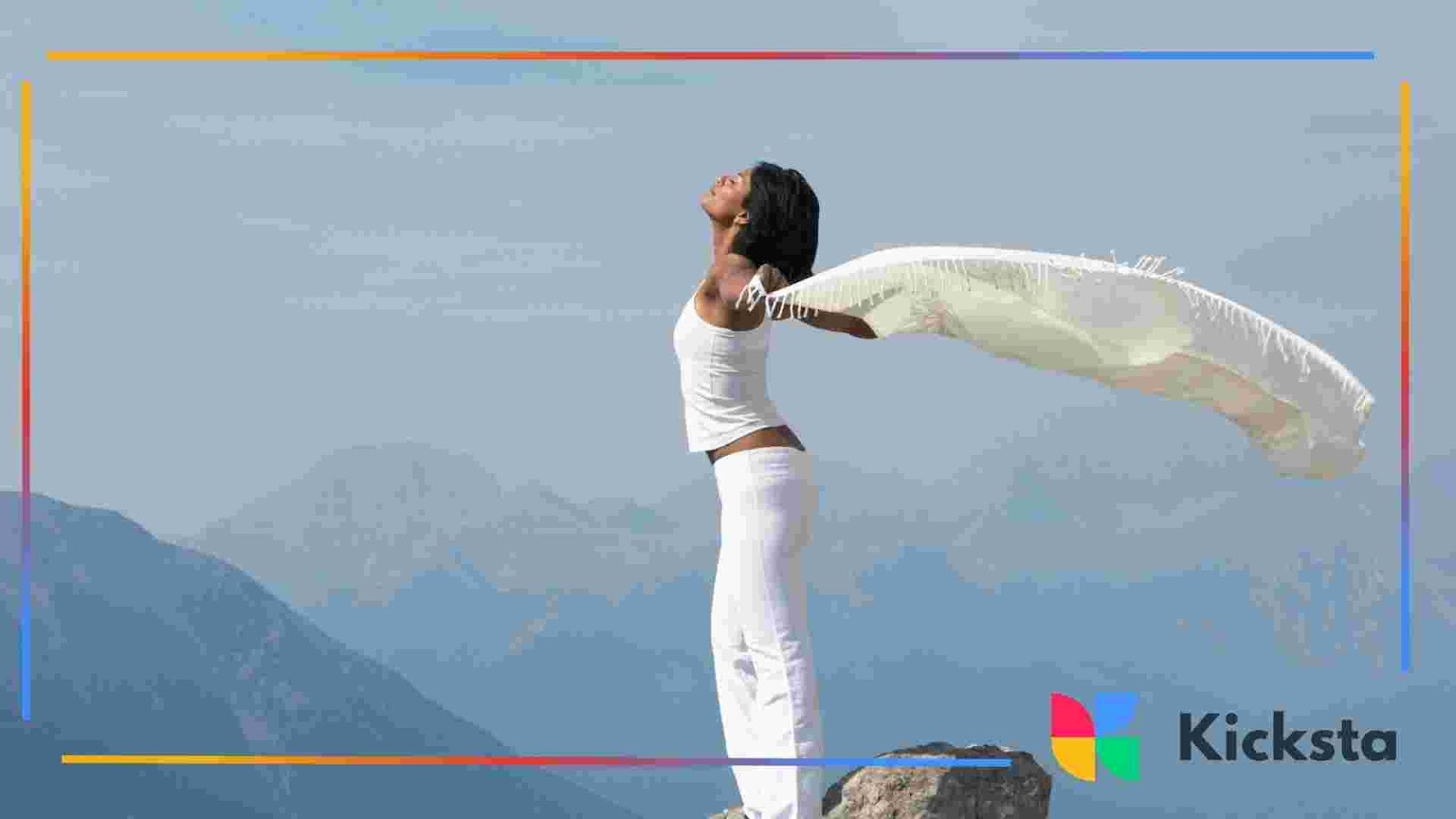 Person standing on a rock with arms open, holding a flowing scarf against a mountain landscape.