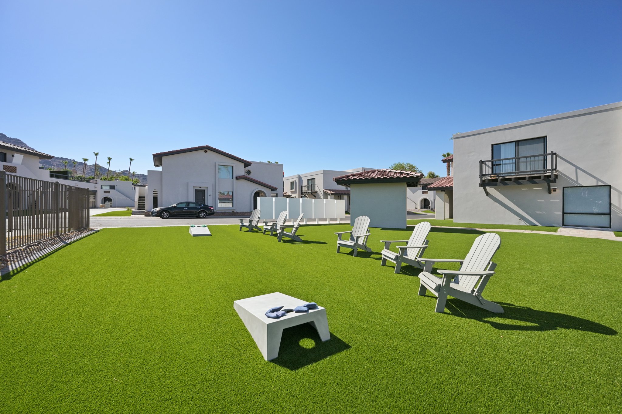 Outdoor game area with a cornhole set and Adirondack chairs on artificial grass, part of the resident amenities at Views at the Peak in Phoenix, AZ.