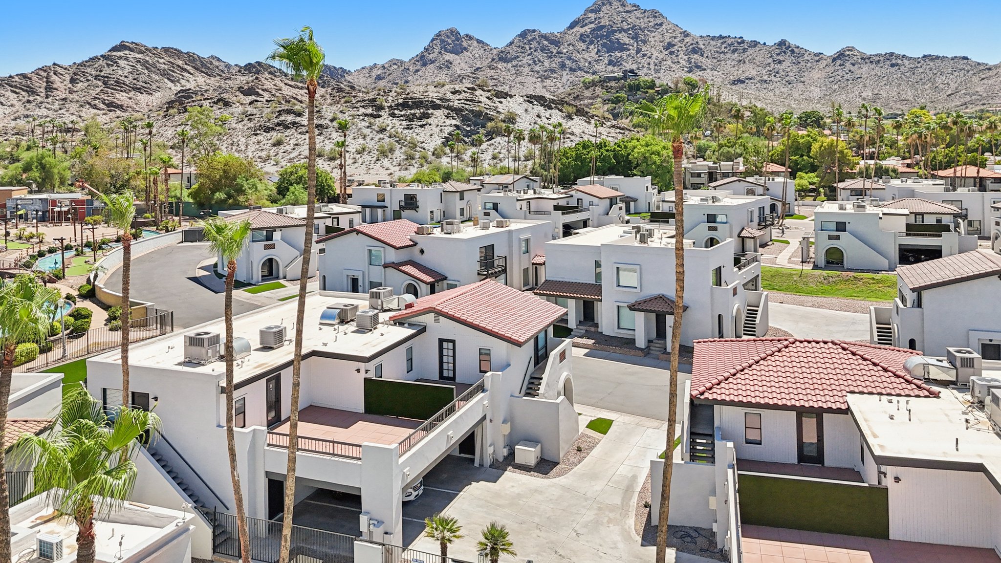 Aerial view of the white townhomes with red tile roofs and palm trees, with desert mountains in the background at Views at the Peak in Phoenix, AZ.