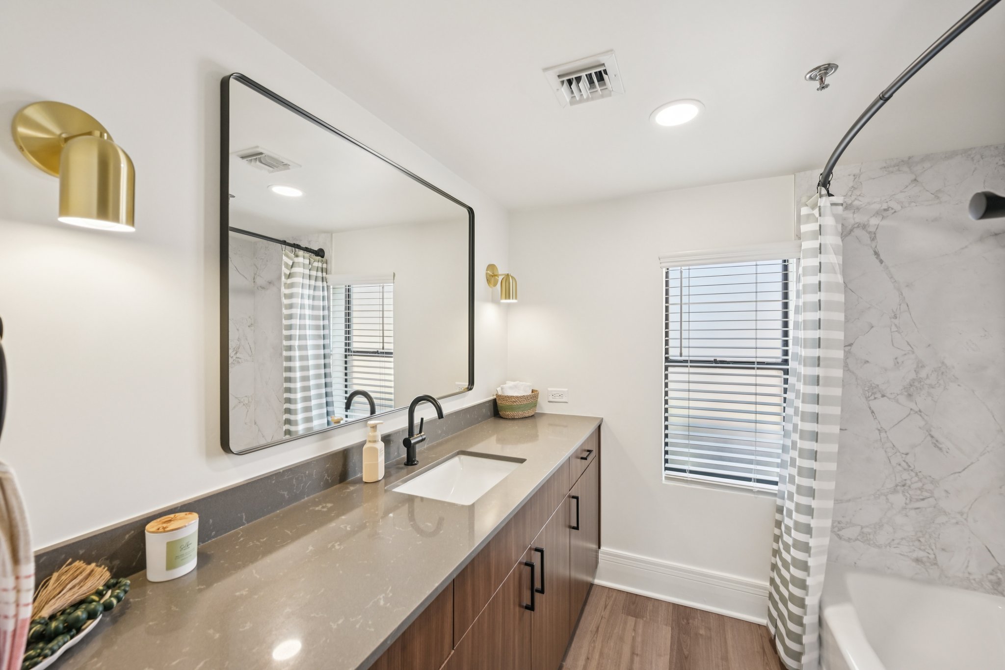 Contemporary bathroom with a single vanity, a large mirror, and a bathtub with a marble-style shower surround at Views at the Peak in Phoenix, AZ.