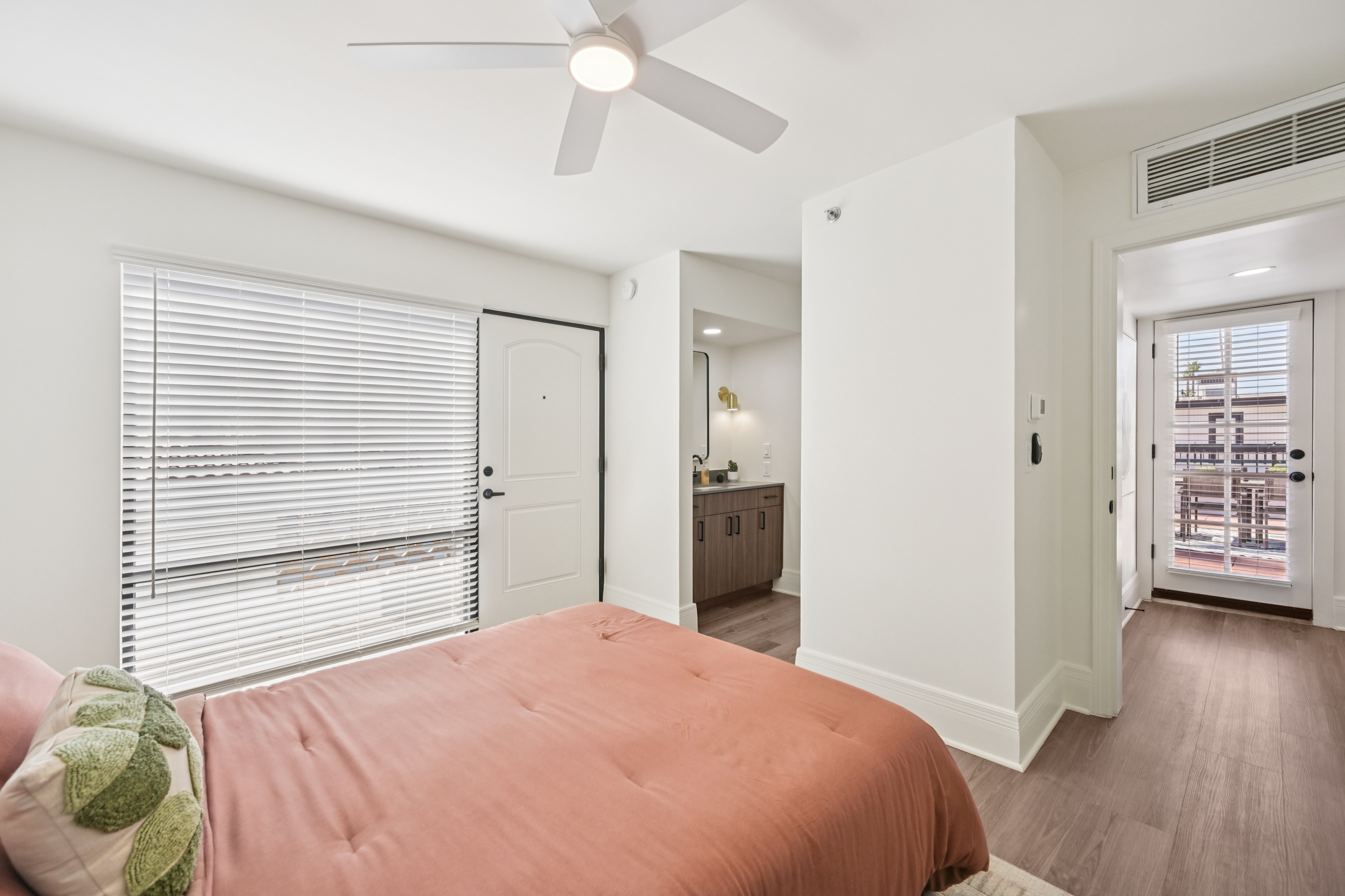 Spacious bedroom with a bed, ceiling fan, and a view into the en-suite bathroom, with a door leading to a patio at Views at the Peak in Phoenix, AZ.