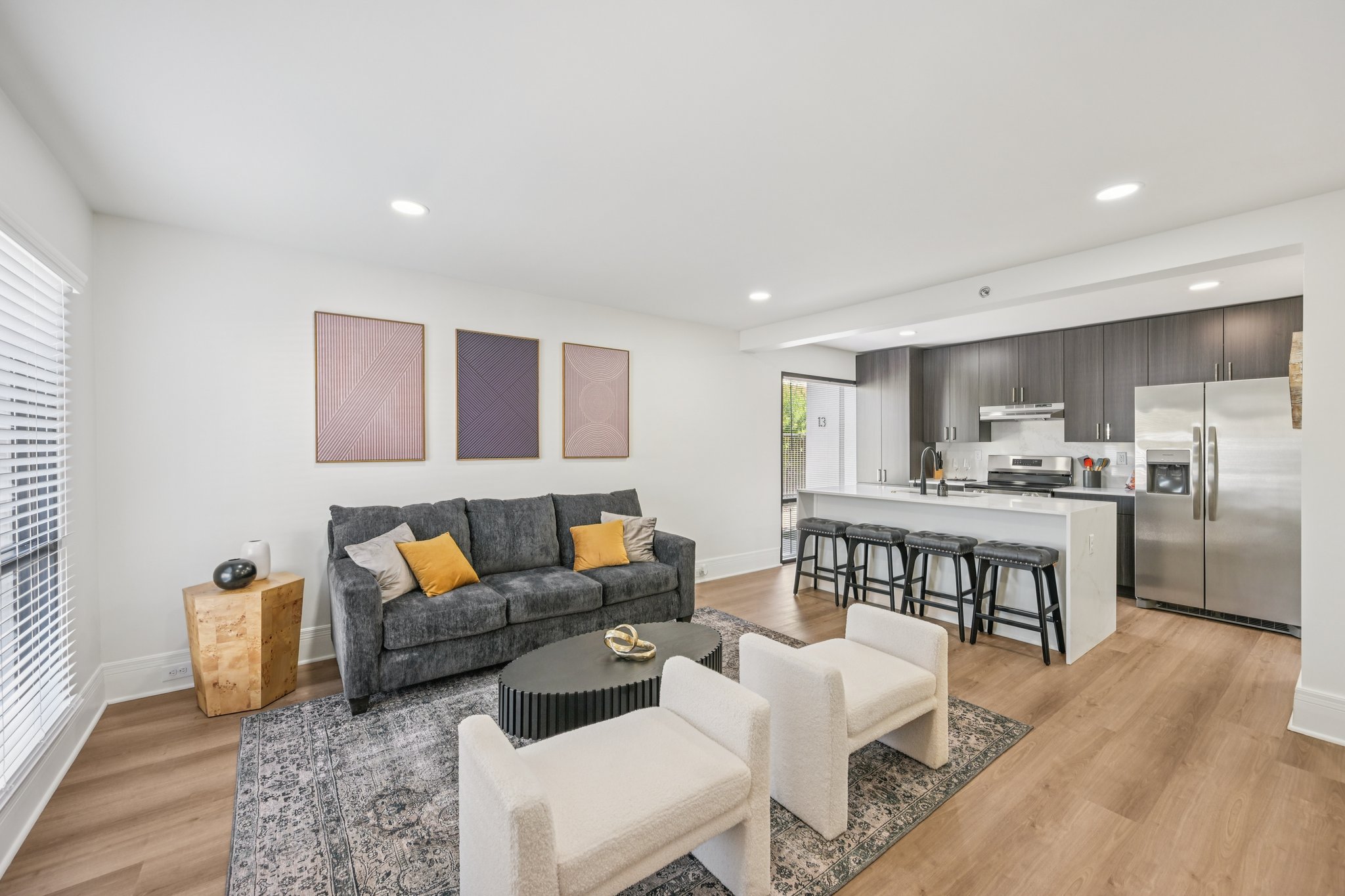 Open-concept living room with a sofa, armchairs, and a view of the modern kitchen with bar seating, at Views at the Peak in Phoenix, AZ.