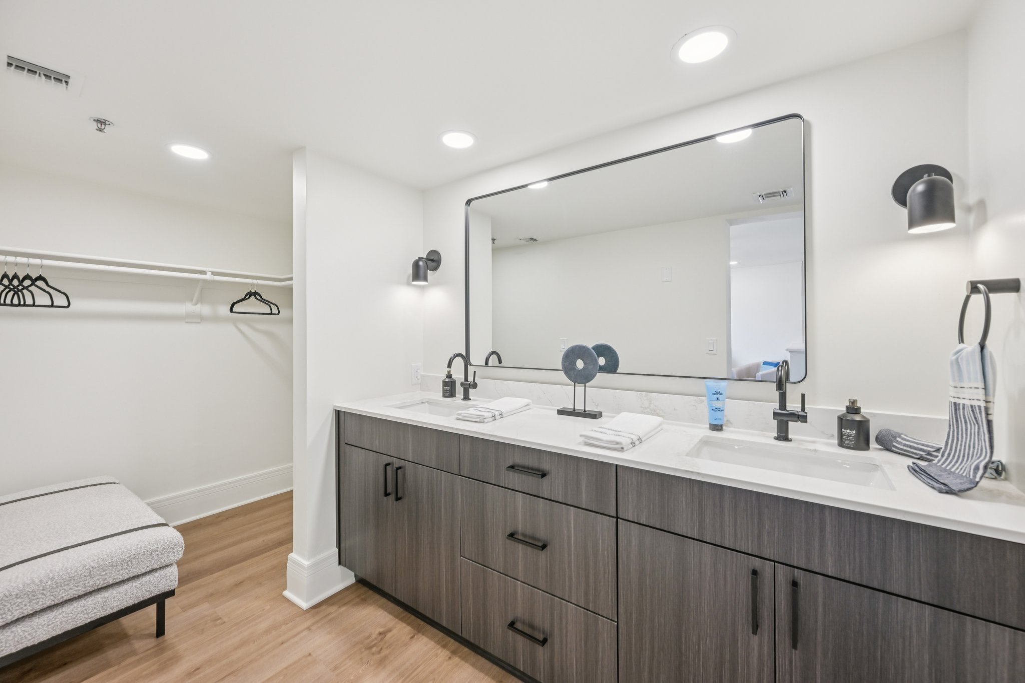Modern bathroom with a double vanity, large mirror, and an adjacent walk-in closet with a bench, in an townhome at Views at the Peak in Phoenix, AZ.