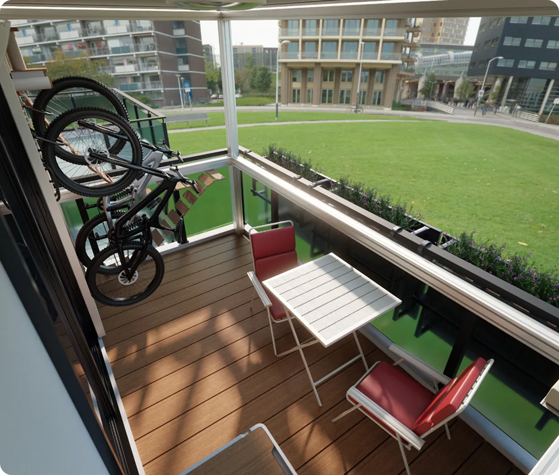 Small balcony with wooden floor, two red cushioned chairs, a white table, and two bicycles mounted on the side railing, overlooking a green lawn and modern buildings.