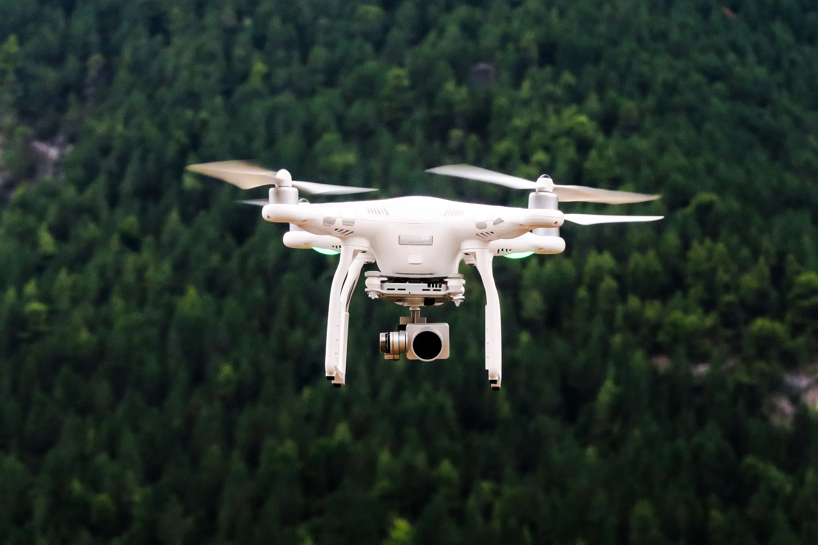 Weiße Drohne fliegt vor dem Hintergrund eines Waldes
