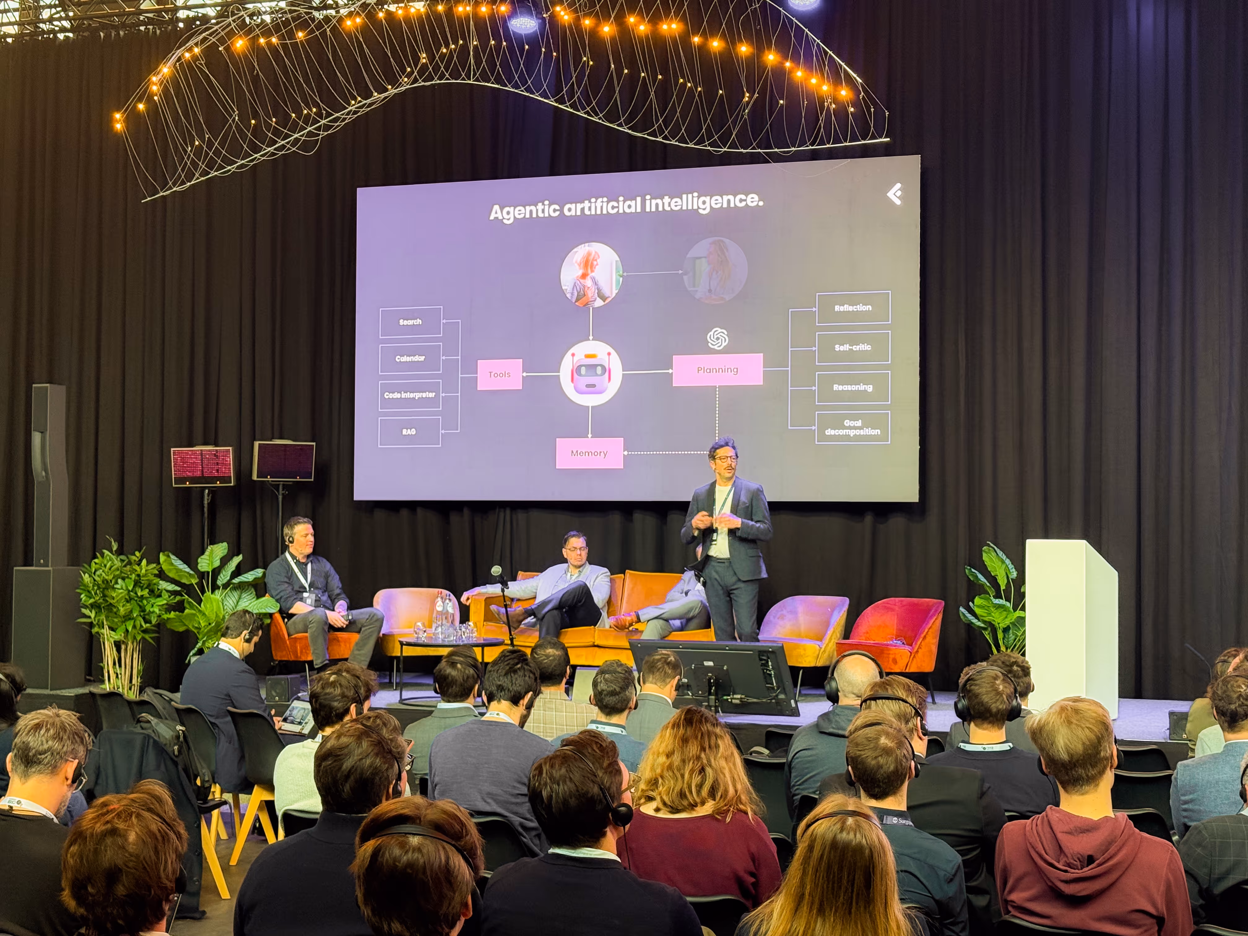 Jan is presenting a slide titled 'Agentic artificial intelligence' to an audience seated in front of a stage with chairs and plants.