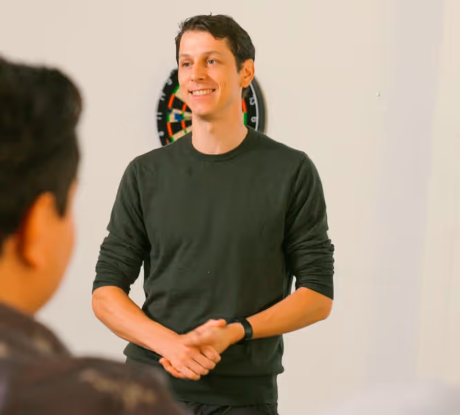 Jeroen smiling standing in front of a dartboard, speaking to an audience.