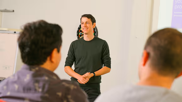 Jeroen Smiling in a dark sweater, giving a presentation to two seated listeners in a meeting room.