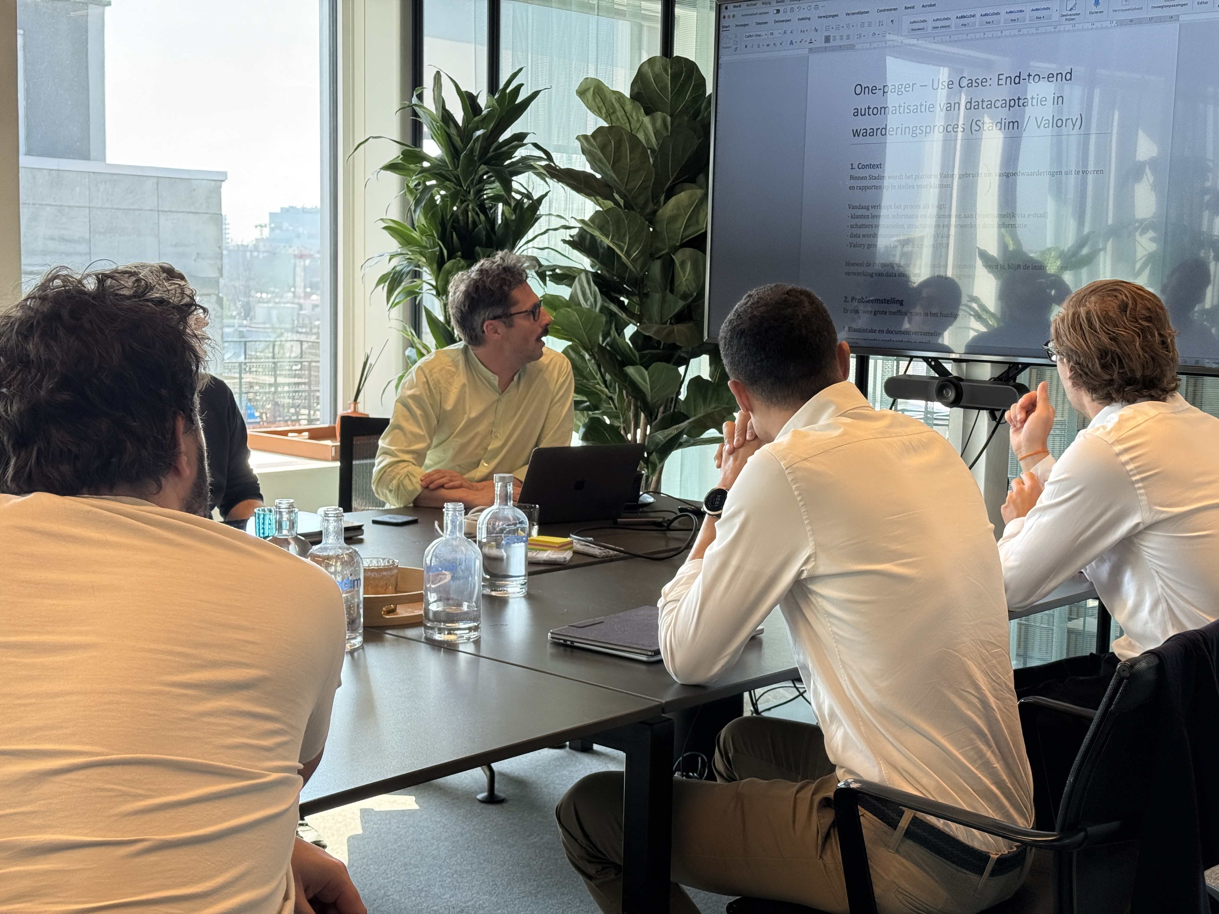 Five men in a meeting room, one presenting a document projected on a large screen.