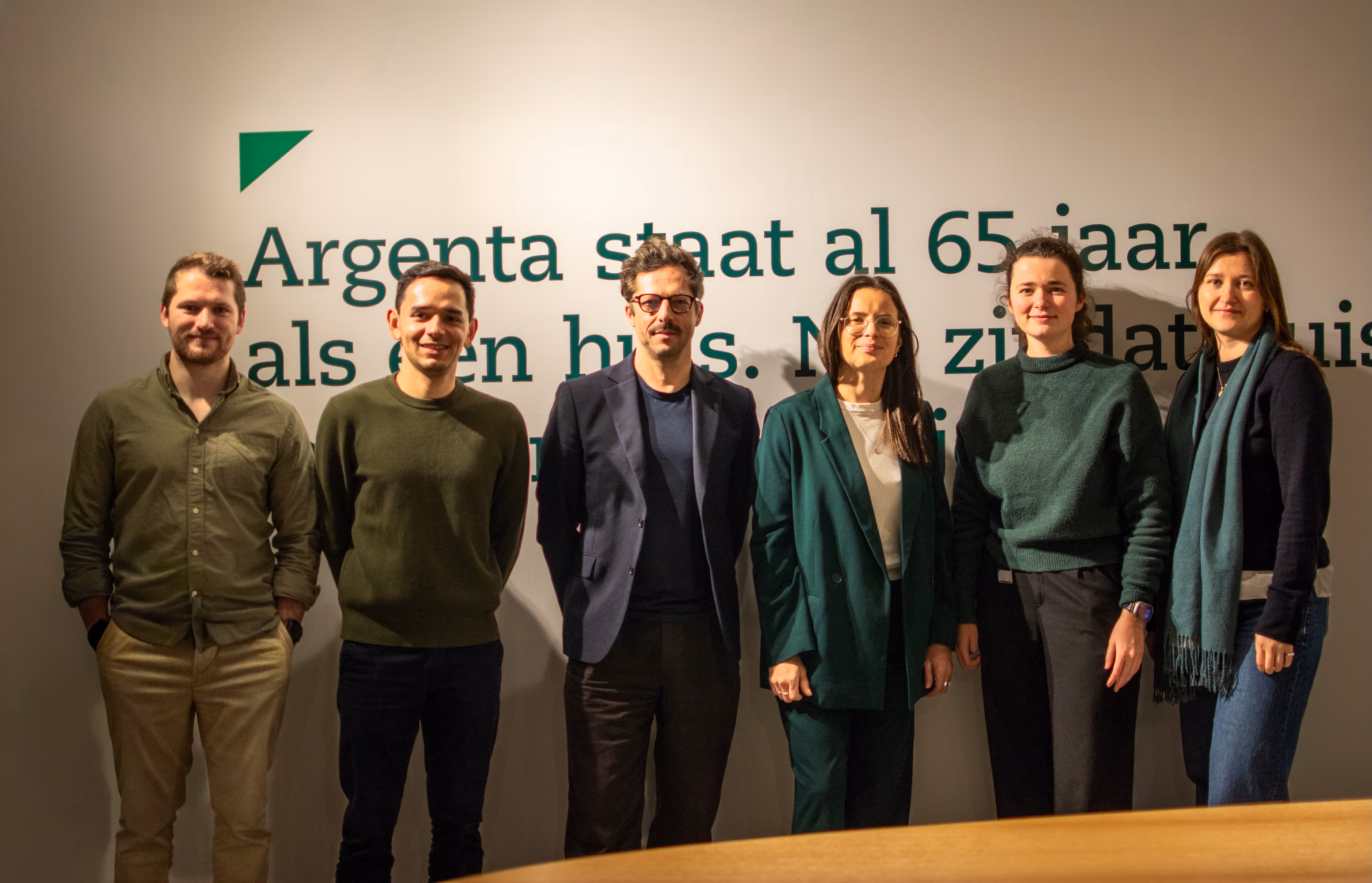 Jan is addressing an audience in a well-lit room with plants and a projection screen.