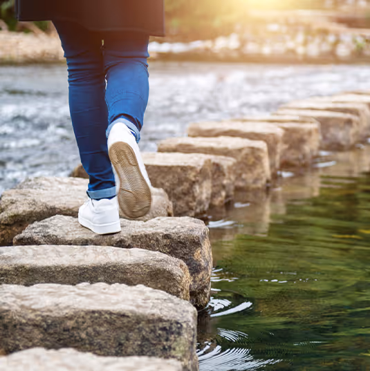Closeup of a person's feet walking on rocks crossing a stream