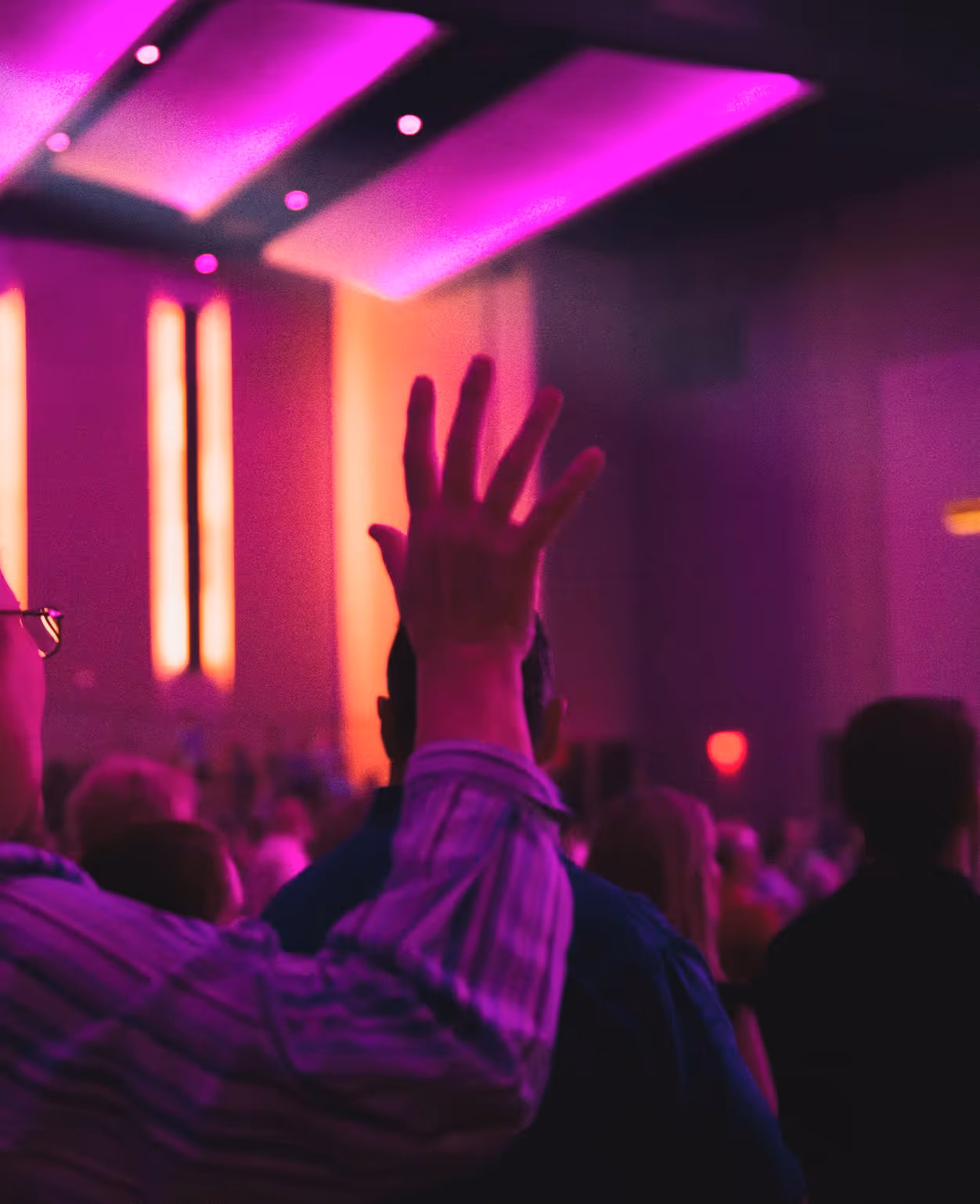 Raised hand at concert with vibrant pink and purple stage lighting