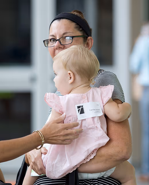 Adult holding baby in pink dress with name tag at event