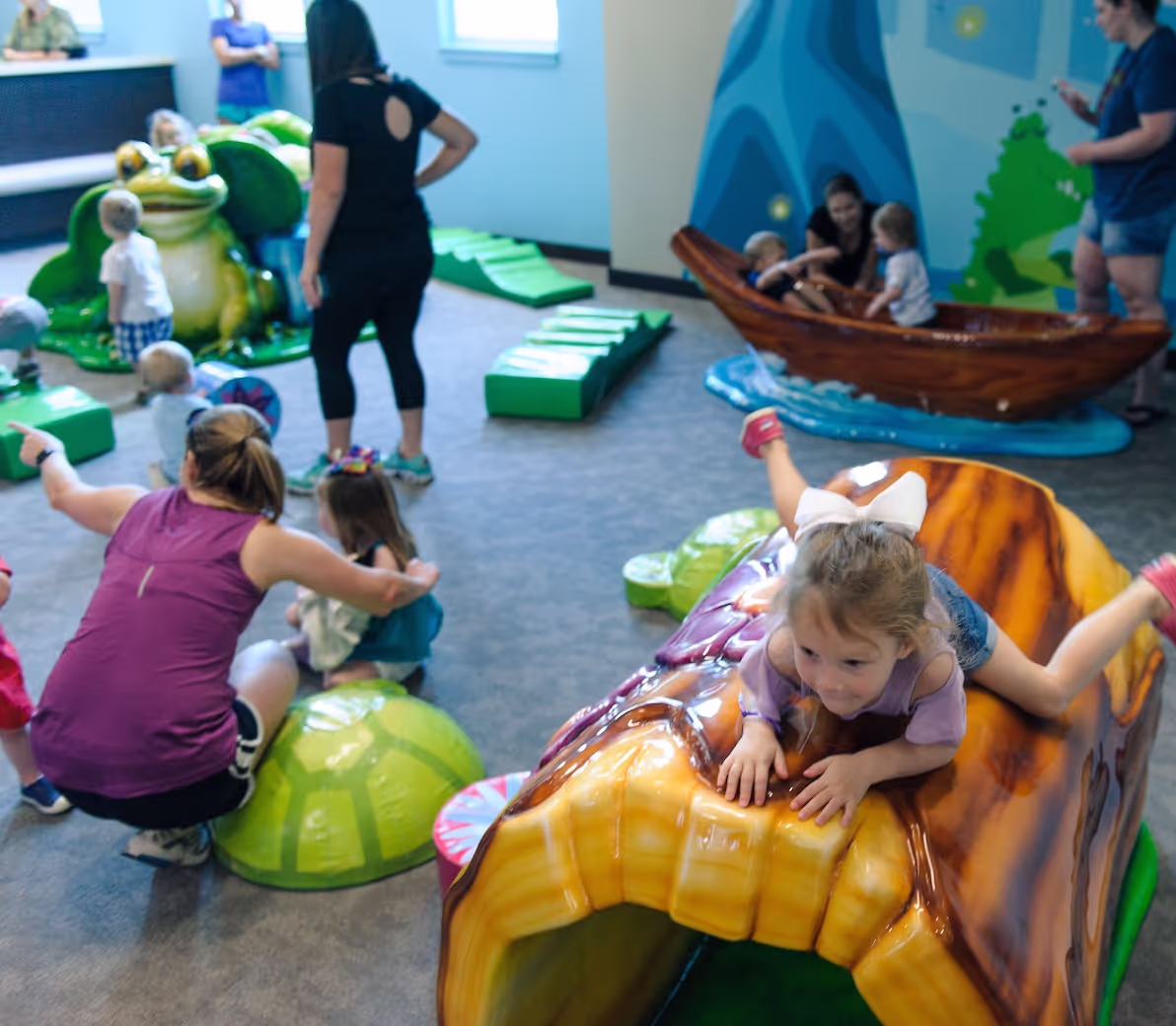 Children play on colorful frog and insect-themed playground equipment