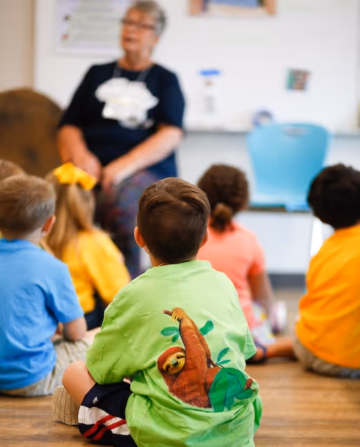 Children sitting on floor listening to teacher in colorful classroom