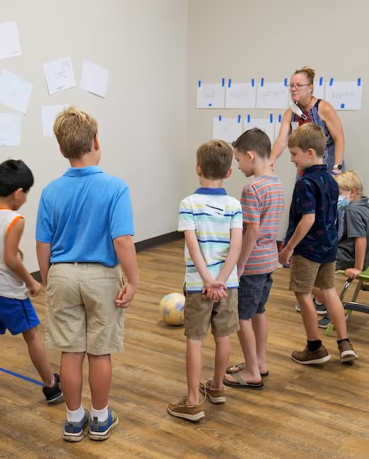 Children in classroom listen to teacher near whiteboard with sticky notes