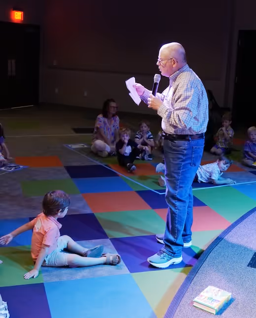 Older speaker reading to children on colorful carpet during storytelling session