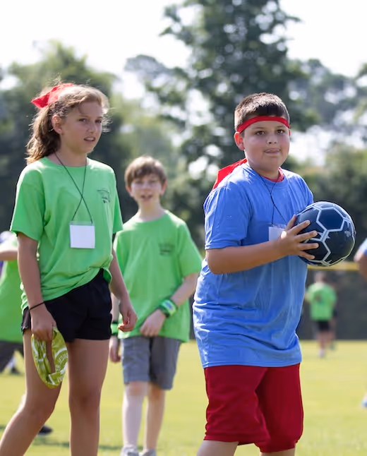 Kids in green and blue shirts prepare for soccer game on sunny field