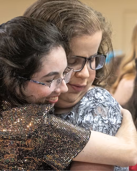 Two people hugging, wearing glasses and sparkly textured clothing
