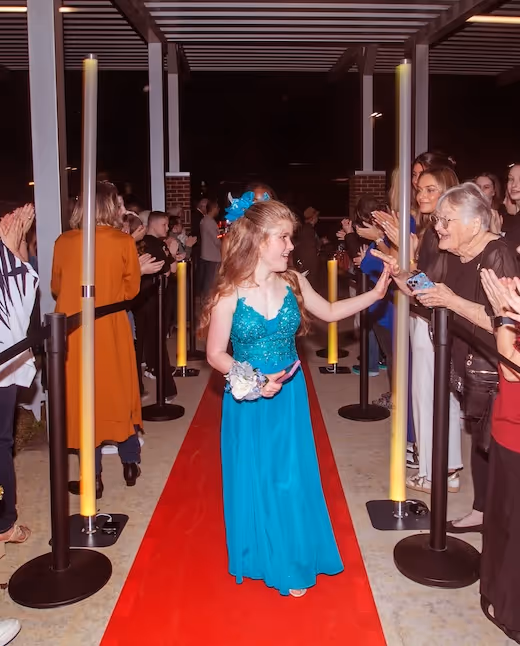 Girl in blue dress walking red carpet with people applauding