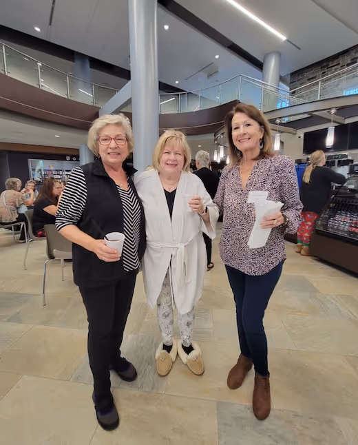 Three women smiling together in a bright, modern indoor space