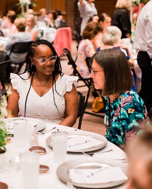 Two women smiling and talking at a formal event with table settings