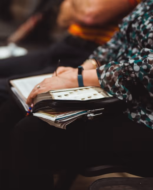 Hand writing in notebook with smartphone and papers nearby