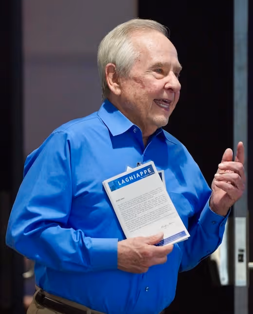 Elderly person in blue shirt laughing while holding a Lagniappe document