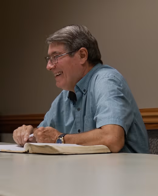 Smiling person in blue shirt studying an open book at a table