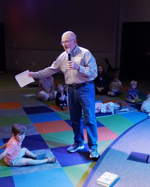 Speaker addressing audience on colorful carpet with children sitting around