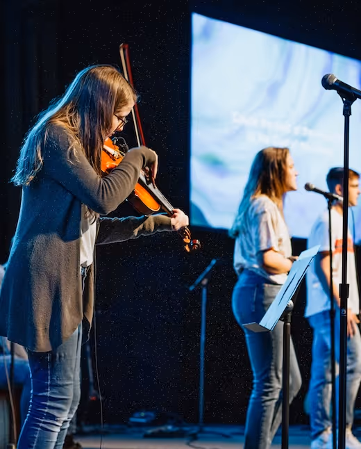 Musician playing violin on stage with singers and microphones