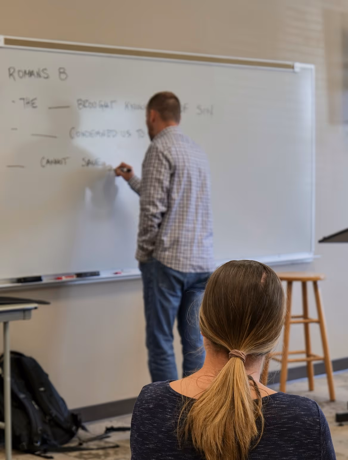 Instructor writing on whiteboard while student listens in classroom