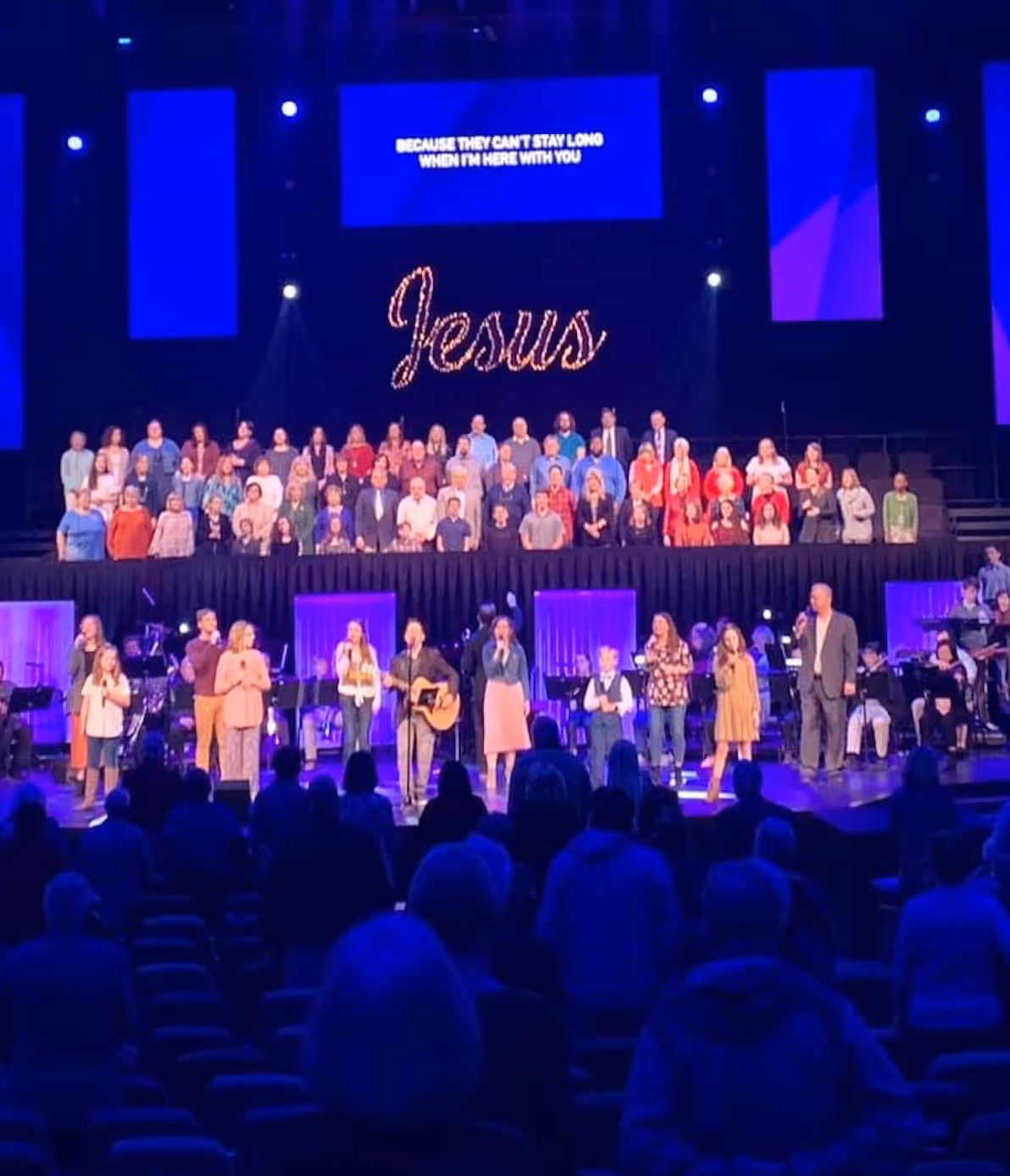 Church choir performing on stage with "Jesus" text in glowing lights