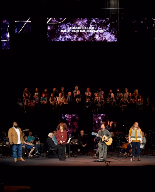 Worship band performing on stage with choir and lyrics projection backdrop