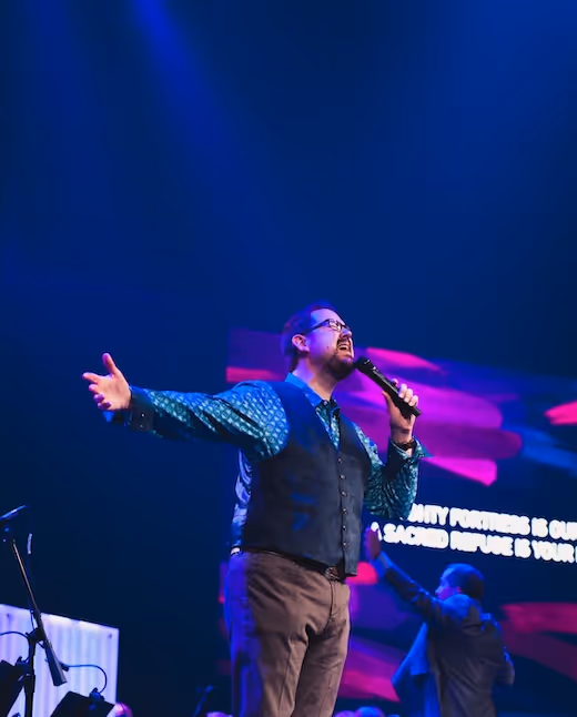 Singer performs passionately on stage with microphone, dramatic blue and pink lighting