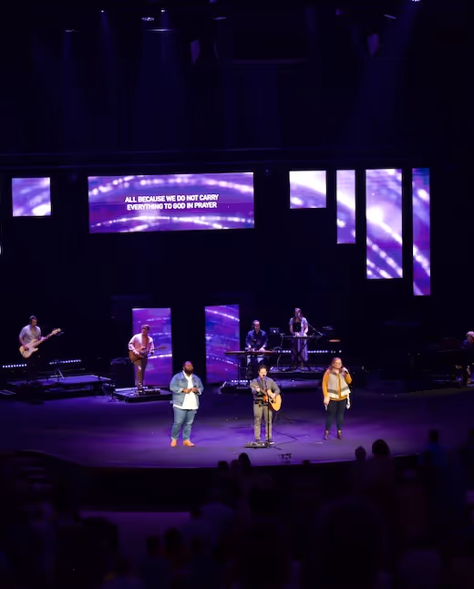 Worship band performing on stage with purple lighting and large video screens