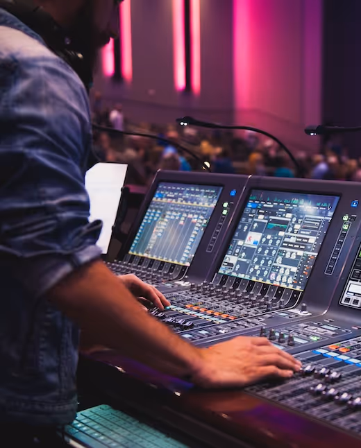 Sound engineer operates digital mixing console during live event with pink lighting