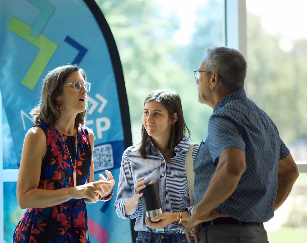 Three professionals conversing near a blue event banner with QR code