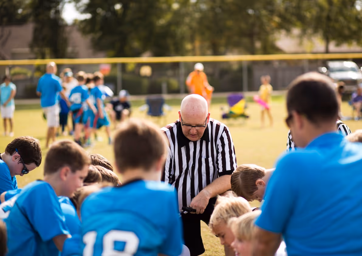 Referee in striped shirt overseeing youth sports game on grassy field