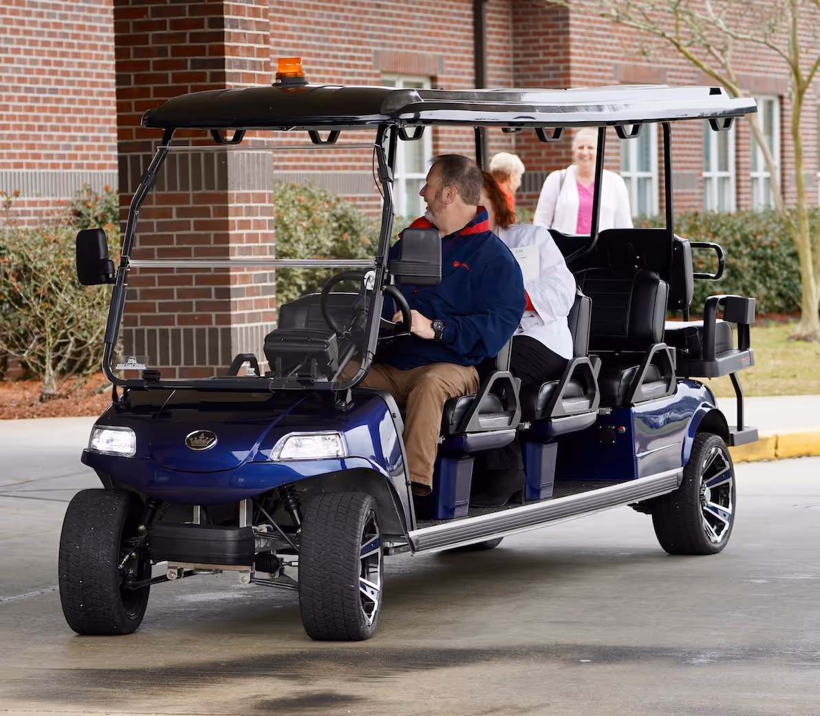 Blue multi-passenger golf cart parked near brick building with people inside