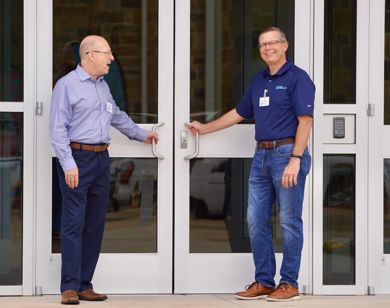 Two businessmen smiling and standing at glass doors