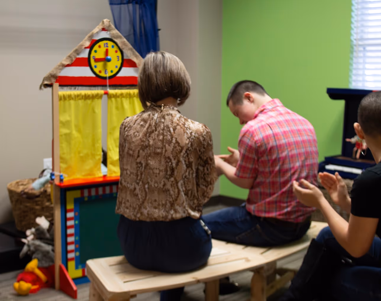 Adults sitting near colorful clock and learning station in classroom