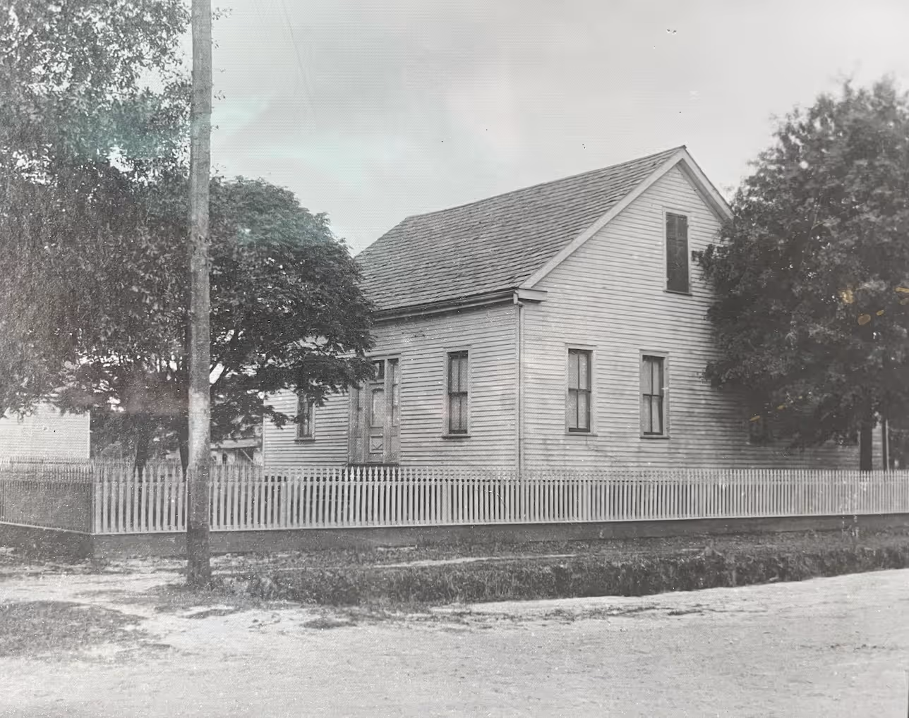 Vintage black and white photo of white wooden house with picket fence