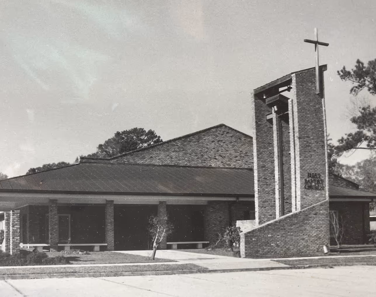 Brick church building with tall bell tower and cross in black and white