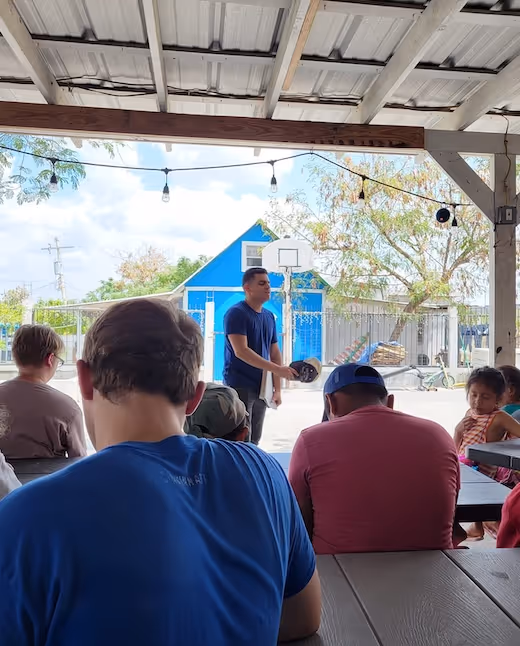 Group listening to speaker under covered patio with blue building background