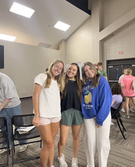 Three smiling friends standing together in an indoor room